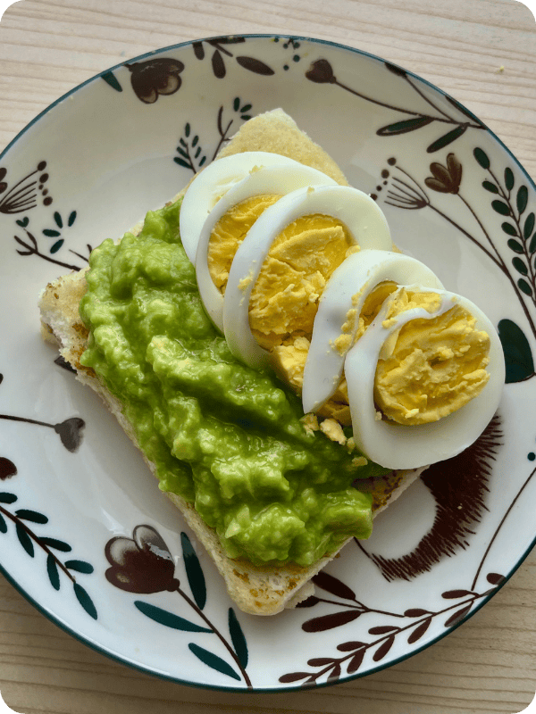Mashed avocado and sliced hard boiled egg on a decorative ceramic plate