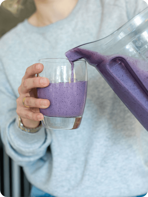 Woman pours a vibrant purple smoothie into a clear glass