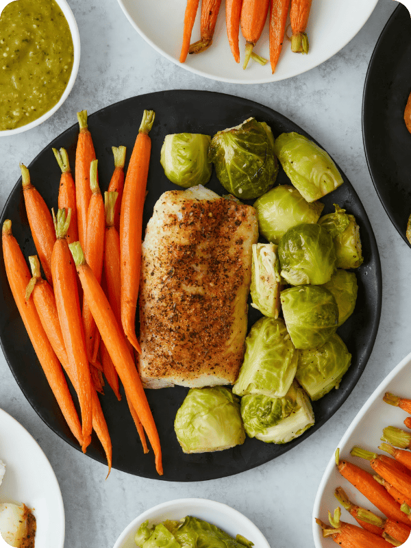 Plate of cooked carrots, fish, and brussels sprouts