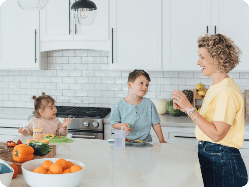 Mom and two toddlers smile in the kitchen