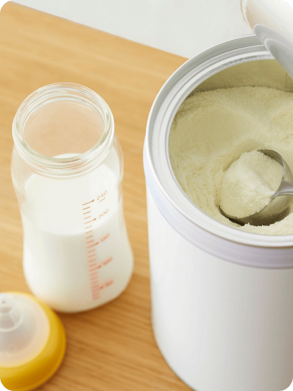 An open canister of infant formula with a glass bottle beside it.