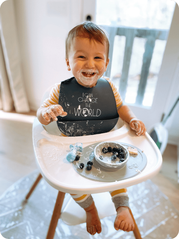 One year old messy with yogurt and berries in their high chair.