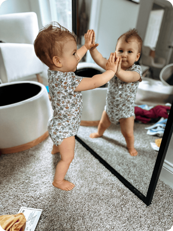 Baby stands at a mirror