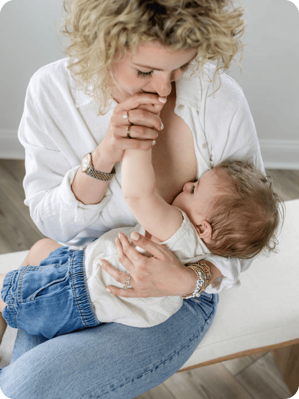 Mother kisses baby's hand during a nursing session