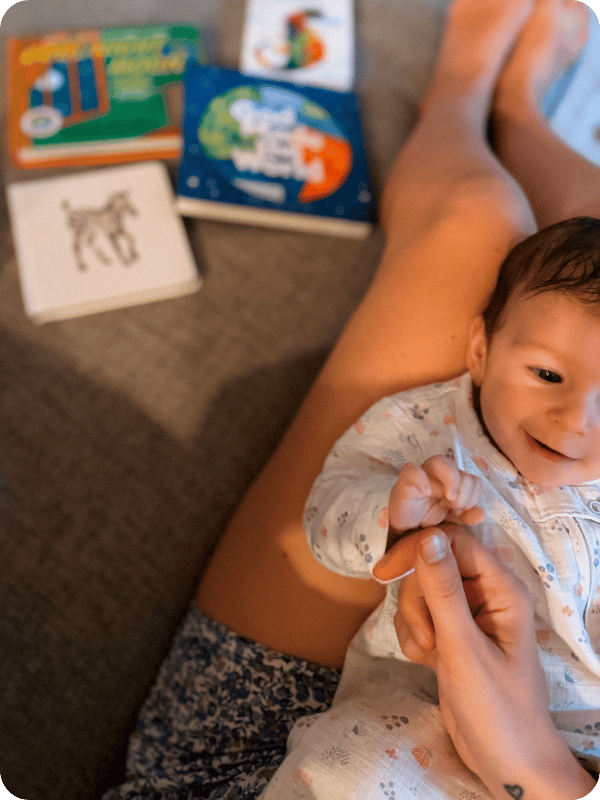 Mom props her nearly 3 month old infant on her legs for face time, with a pile of books in the background