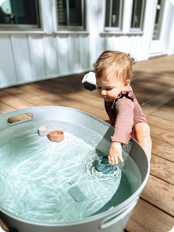 toddler engaging in water play with a big bucket and scoops
