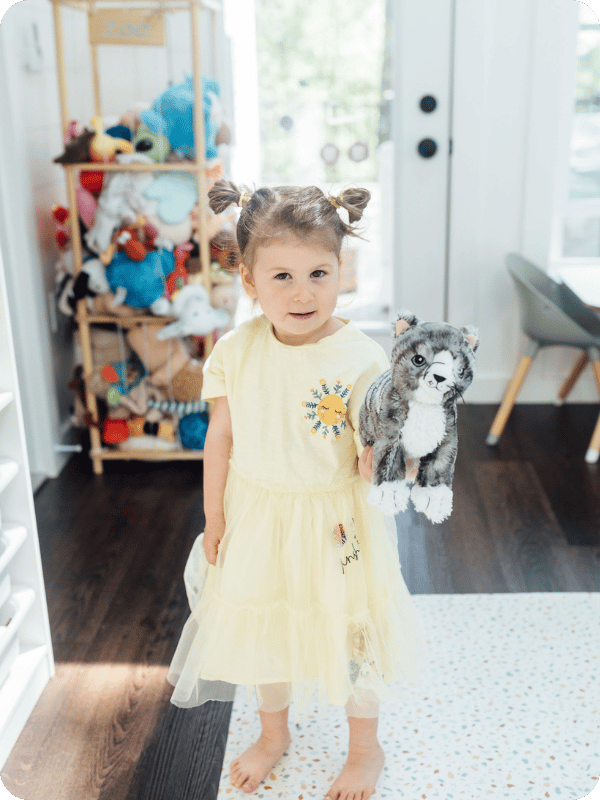 3 year old in a yellow dress shows the camera her cat stuffed animal