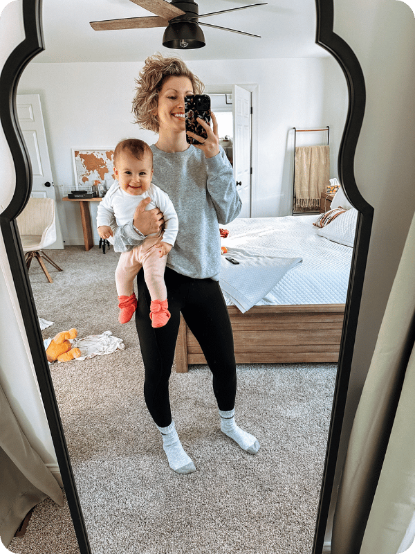 Mom and baby smile in the mirror, wearing comfy clothes.