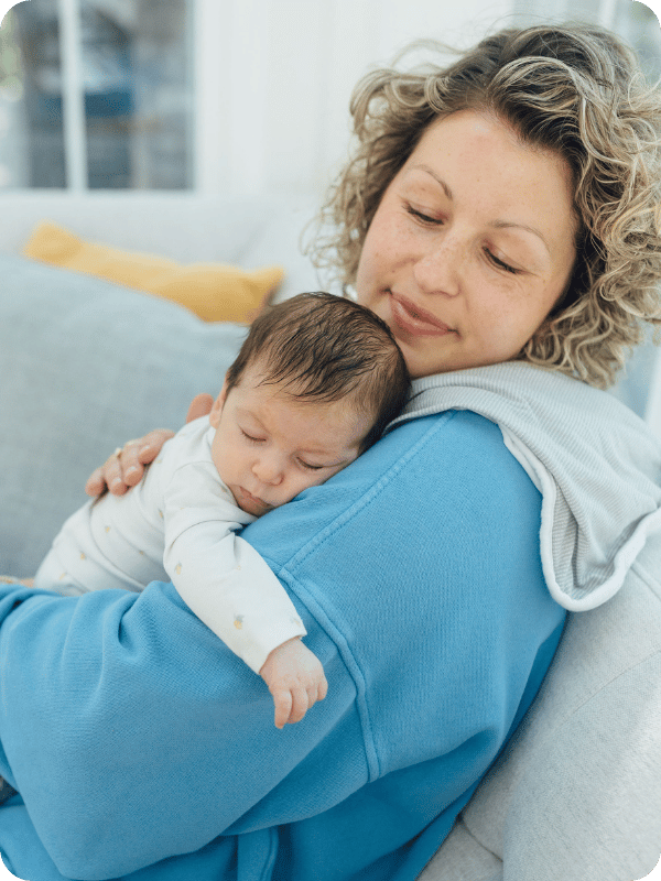 Mom holds baby against her shoulder with a burp cloth under her. Both have their eyes closed and are relaxed and resting
