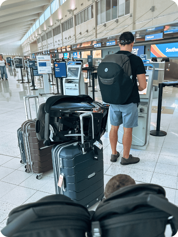 dad in an airport with luggage, car seats, and travel stroller