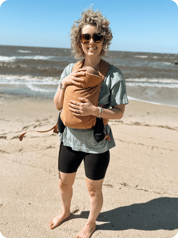 mom using wildbird aerial buckle baby carrier on the beach while traveling