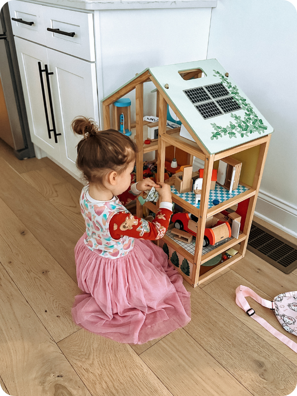 toddler girl playing with Hape dollhouse