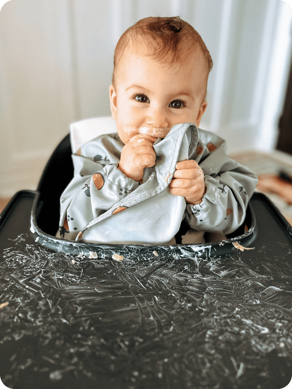Baby wears a bib in the high chair, which is smeared with pureed food.