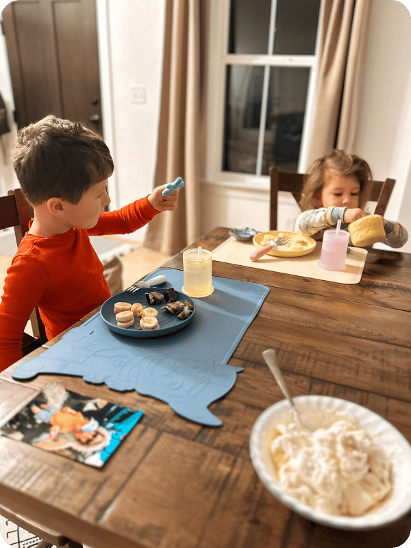 Toddlers eat breakfast at the dining room table.