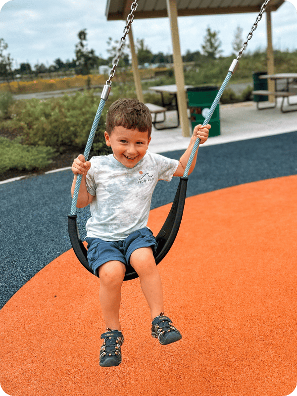 Preschooler swings on the playground at the park, smiling at the camera.