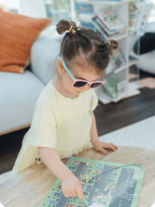 Penelope plays with a magnetic puzzle in the play room, wearing her sunglasses.