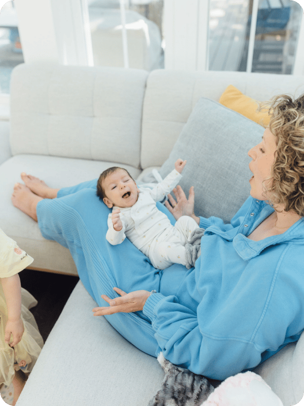 Young baby resting on mom's legs smiles and plays with mom.