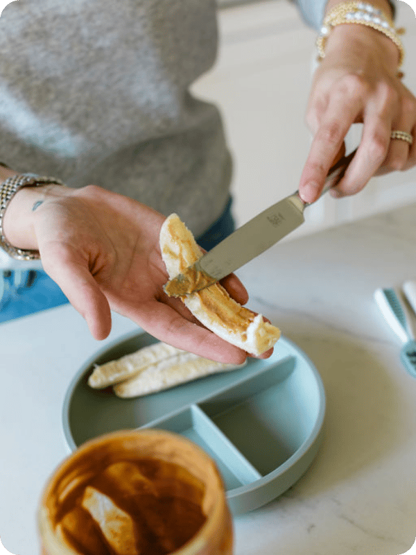 Mom spreads peanut butter on a slice of banana for baby.