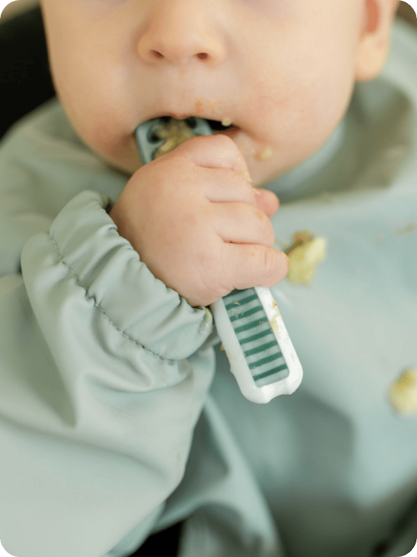 Baby uses a spoon to eat a bite of mashed food.