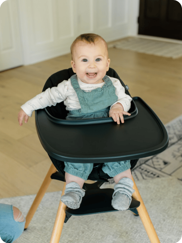 Infant smiles while sitting in her high chair.