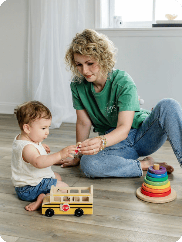 Mom and toddler play with a wooden school bus toy.