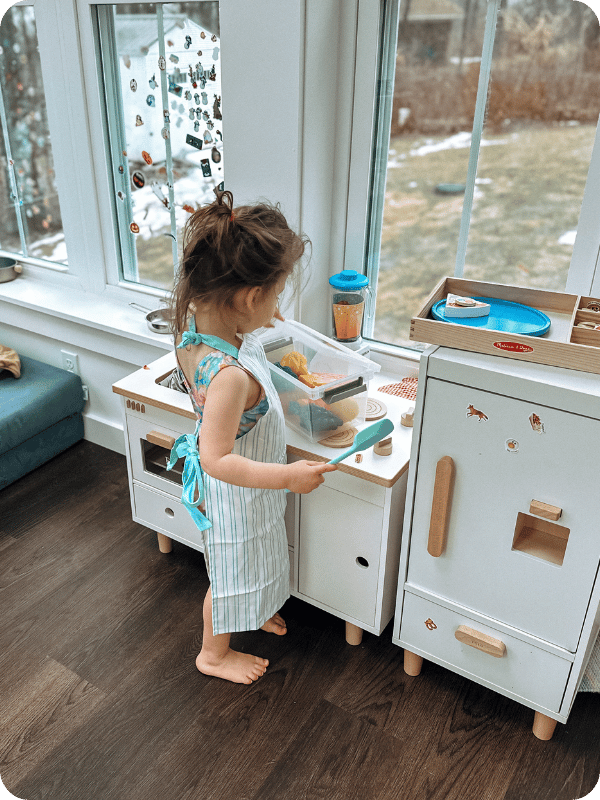 toddler in apron pretend playing in a play kitchen