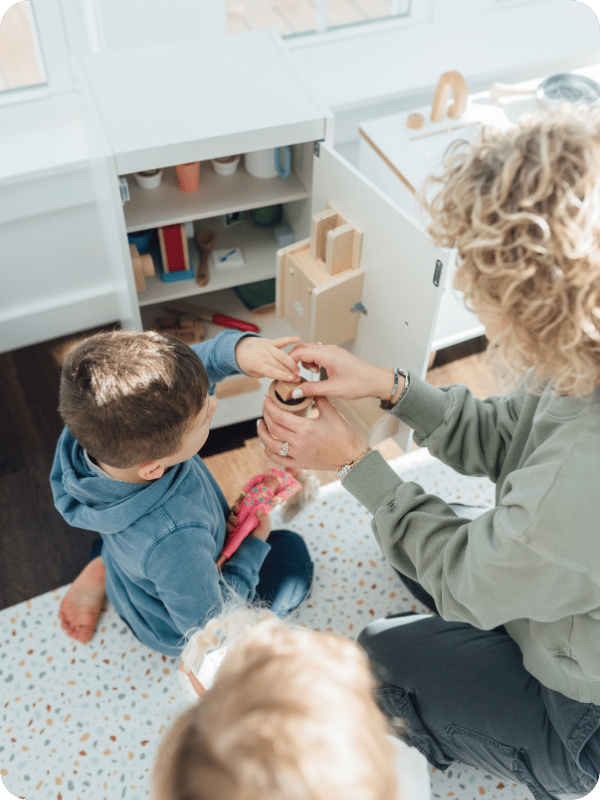Mom and toddlers play with pretend kitchen and food.