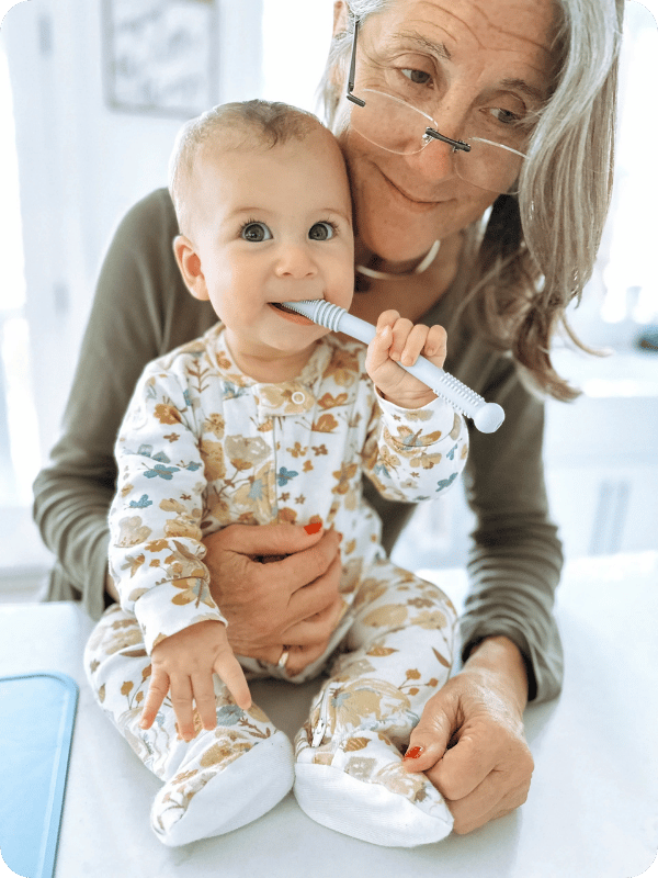 Baby smiles while chewing on a teether, being held by grandma.