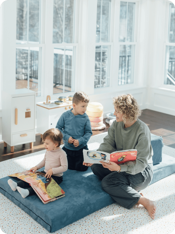 Mom and toddlers read books together on a play couch.