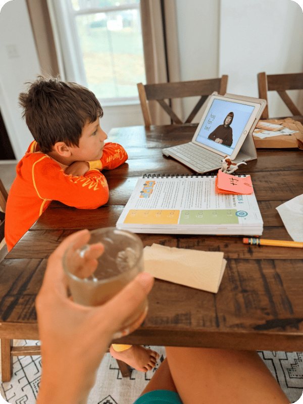 Preschooler does a homeschool lesson at the dining room table beside his mom.