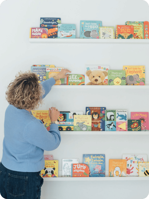 Mom picks a book off the bookshelves.