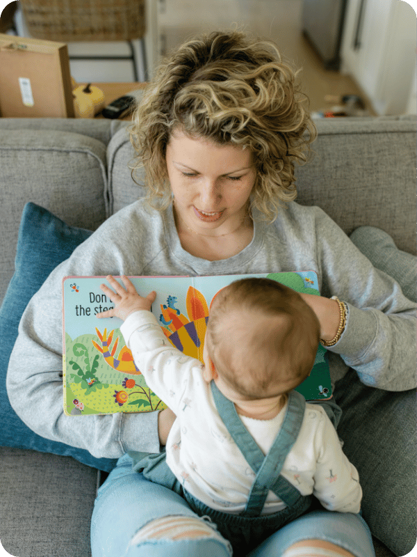 Mom and baby read a book together, with baby propped in mom's lap facing her so they can look at each other while interacting.