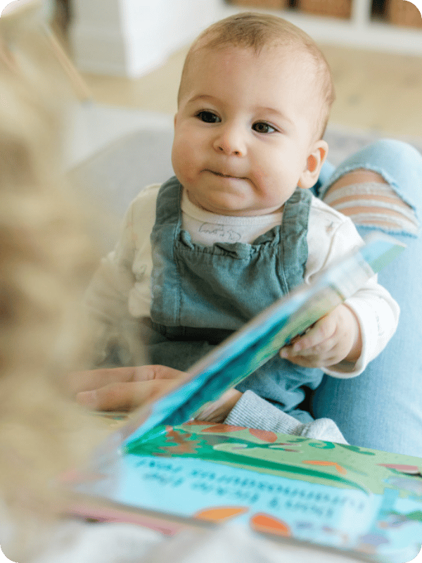 Baby looks at mom while turning a book page.
