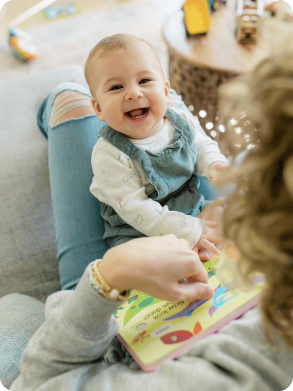 Infant sits in her mom's lap and smiles at the camera.