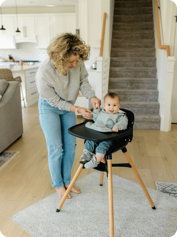 baby sitting in high chair with a splat mat underneath
