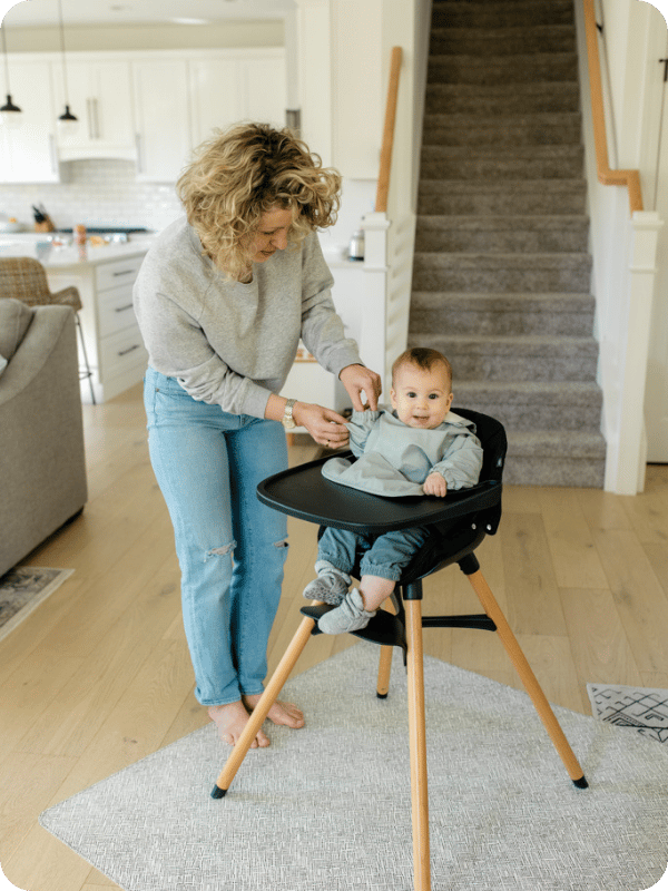 Mom helps get baby ready for a meal in the high chair