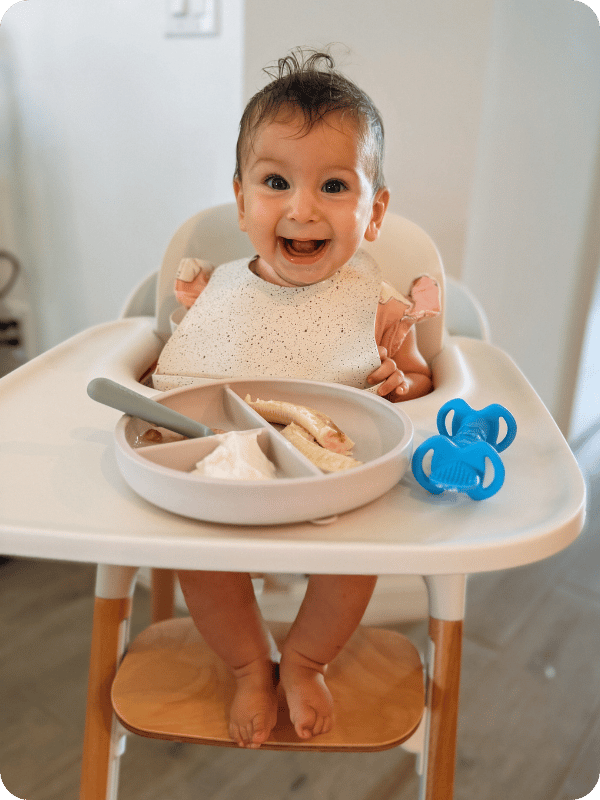 Baby smiles in the high chair while trying new foods