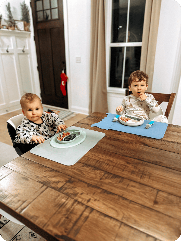 Baby eats dinner at the table with their older sibling