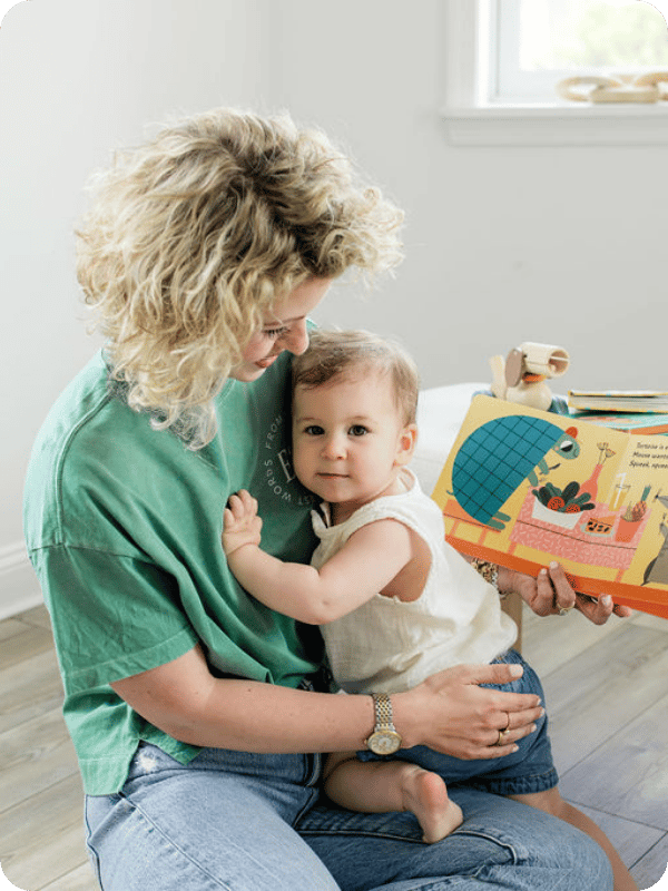 Toddler looks at the camera and sits on mom's lap to read a book